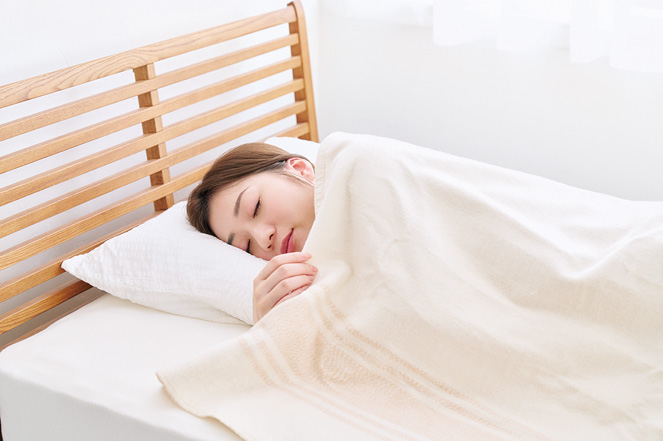 掛け毛布として使う ベッドで電気毛布を掛けて眠る女性|掛け毛布として使用