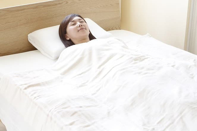 ふんわり柔らかな手触り ベッドで電気毛布を肩にかけてくつろぐ女性|ふんわり柔らかなオーガニックコットン毛布
